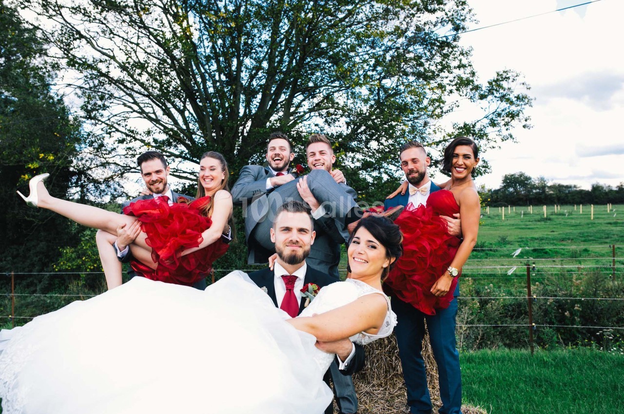 Un groupe de jeunes adultes en tenue de mariage pose joyeusement dans un cadre champêtre.