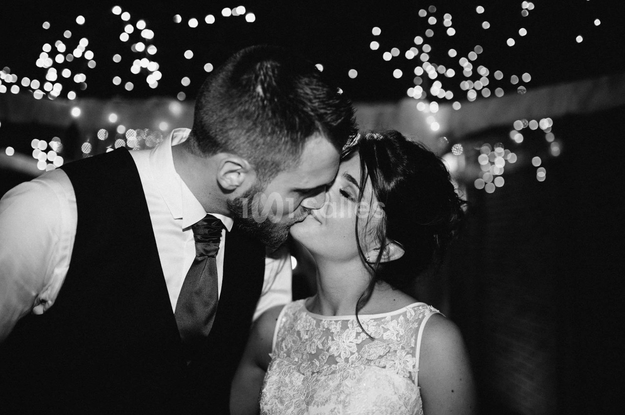 Un couple s'embrasse lors d'une soirée, entouré de guirlandes lumineuses en arrière-plan.