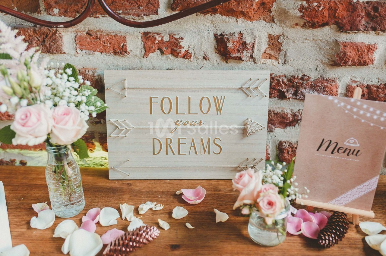Panneau en bois ’Follow your dreams’ entouré de fleurs, pétales et décorations sur une table en bois devant un mur de…