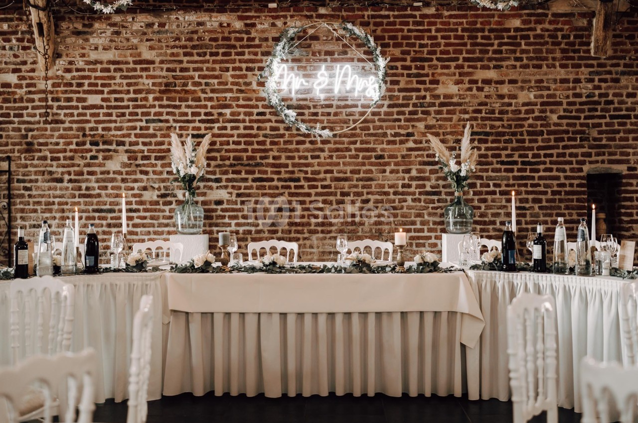 Table de réception élégamment décorée avec nappes blanches, bougies, fleurs et mur de briques en arrière-plan.