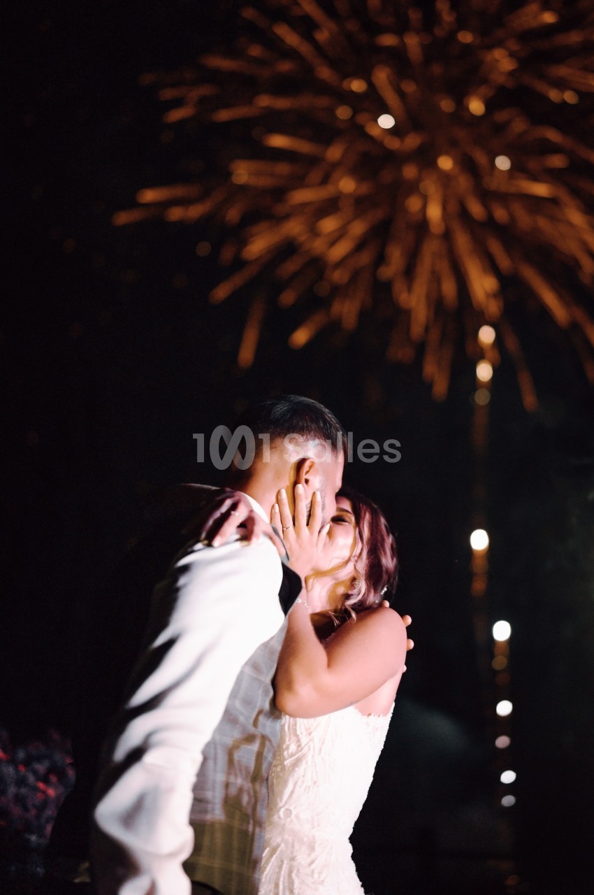 Un couple s'embrasse sous un ciel illuminé par des feux d'artifice.