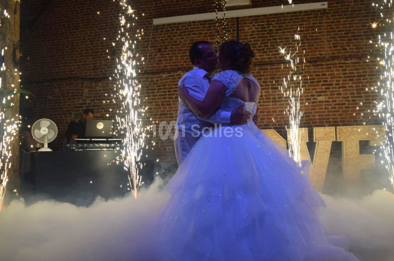 Un couple danse au milieu de fumée et de gerbes d'étincelles, dans une salle en briques avec un DJ en arrière-plan.