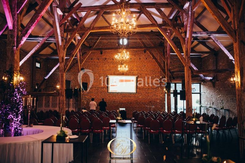 Salle de réception avec poutres apparentes, chaises alignées, écran de projection et lustres suspendus.