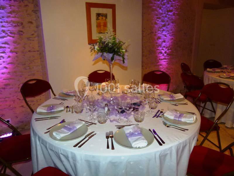 Table ronde élégamment dressée avec nappes blanches, vaisselle raffinée, serviettes pliées et centre de table floral.