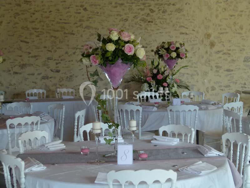 Salle de réception décorée avec des tables dressées, nappes blanches et centres de table fleuris dans des tons roses.