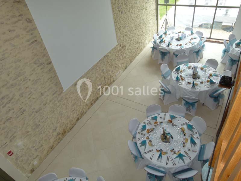 Salle de réception avec tables rondes dressées pour un événement, décorées de nappes blanches et nœuds bleus.