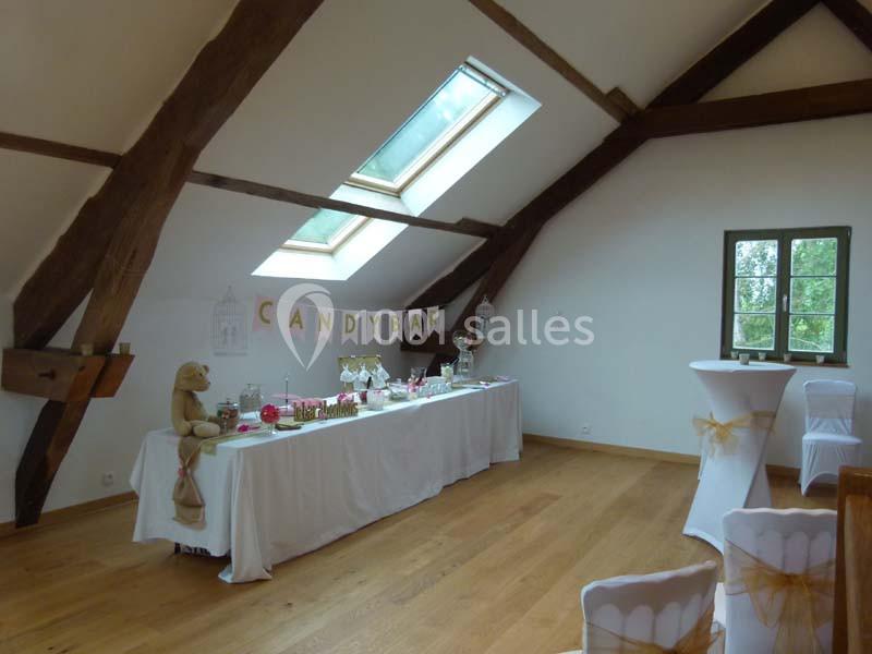 Salle lumineuse avec poutres apparentes, table décorée pour un candy bar sous une fenêtre de toit.