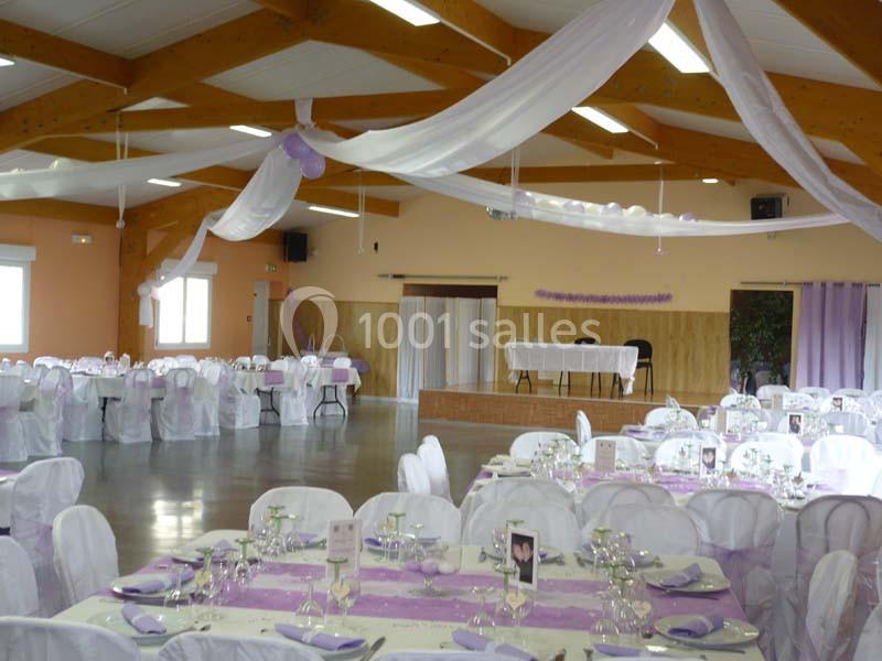 Salle de réception décorée avec des nappes blanches et violettes, des guirlandes suspendues et des tables dressées.