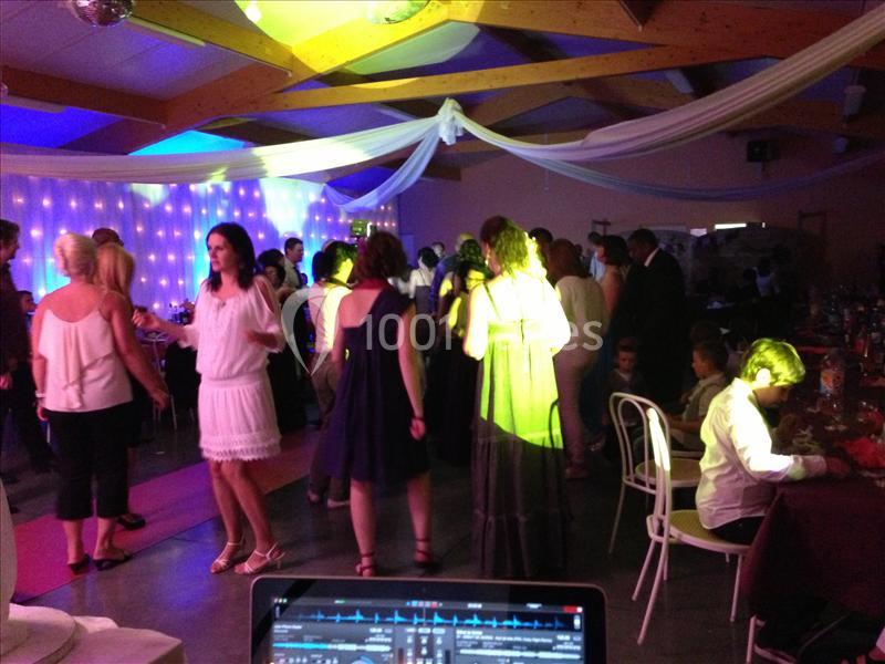 Des personnes dansent et discutent dans une salle décorée pour une fête, éclairée par des lumières colorées.