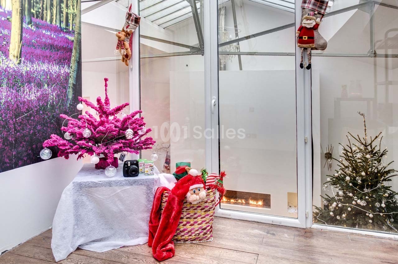 Décoration de Noël avec un sapin rose, une cheminée allumée et des chaussettes suspendues près d'une fenêtre.