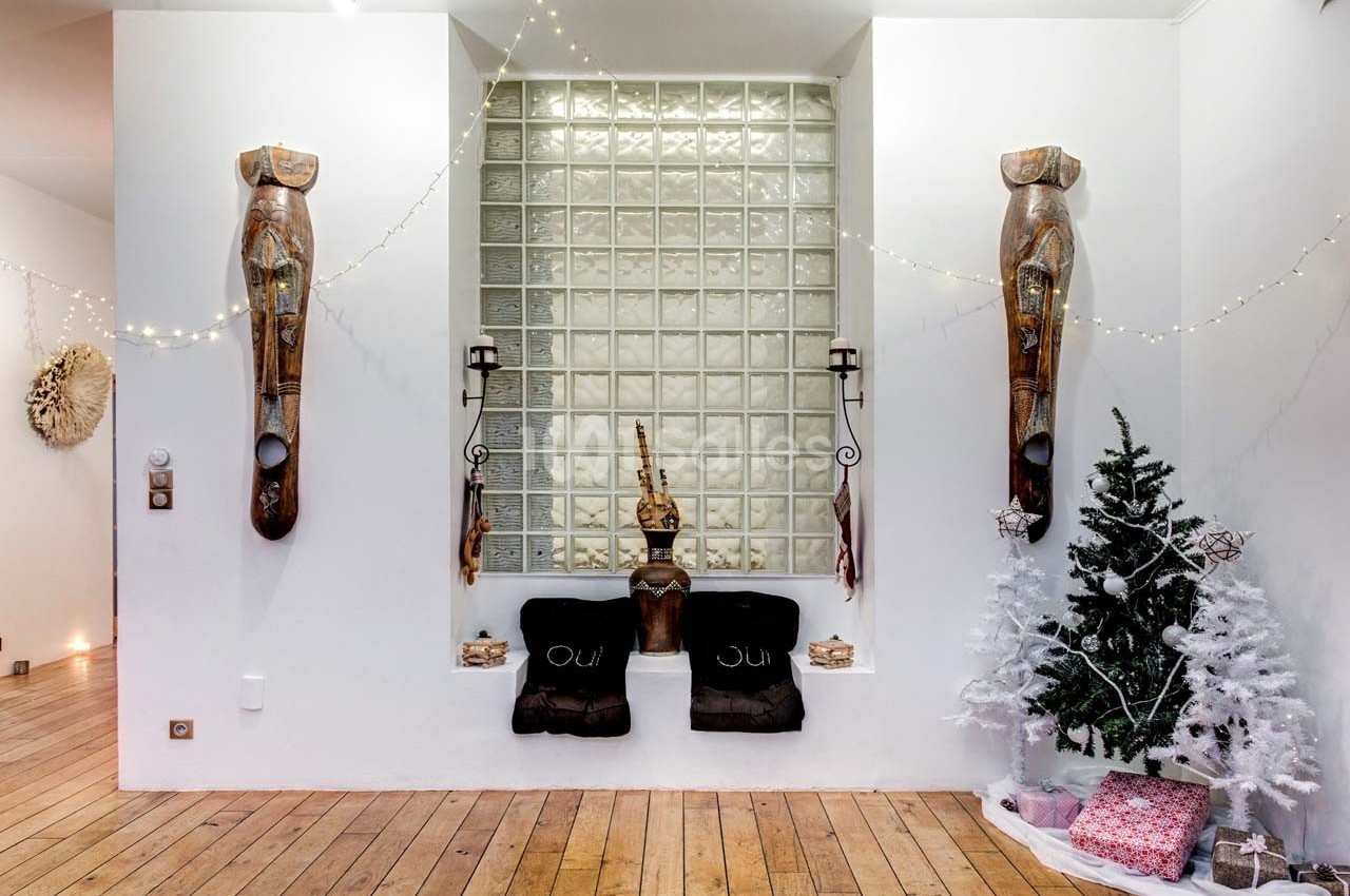 Niche murale décorée avec sculptures en bois, coussins noirs, sapin blanc et guirlandes lumineuses.