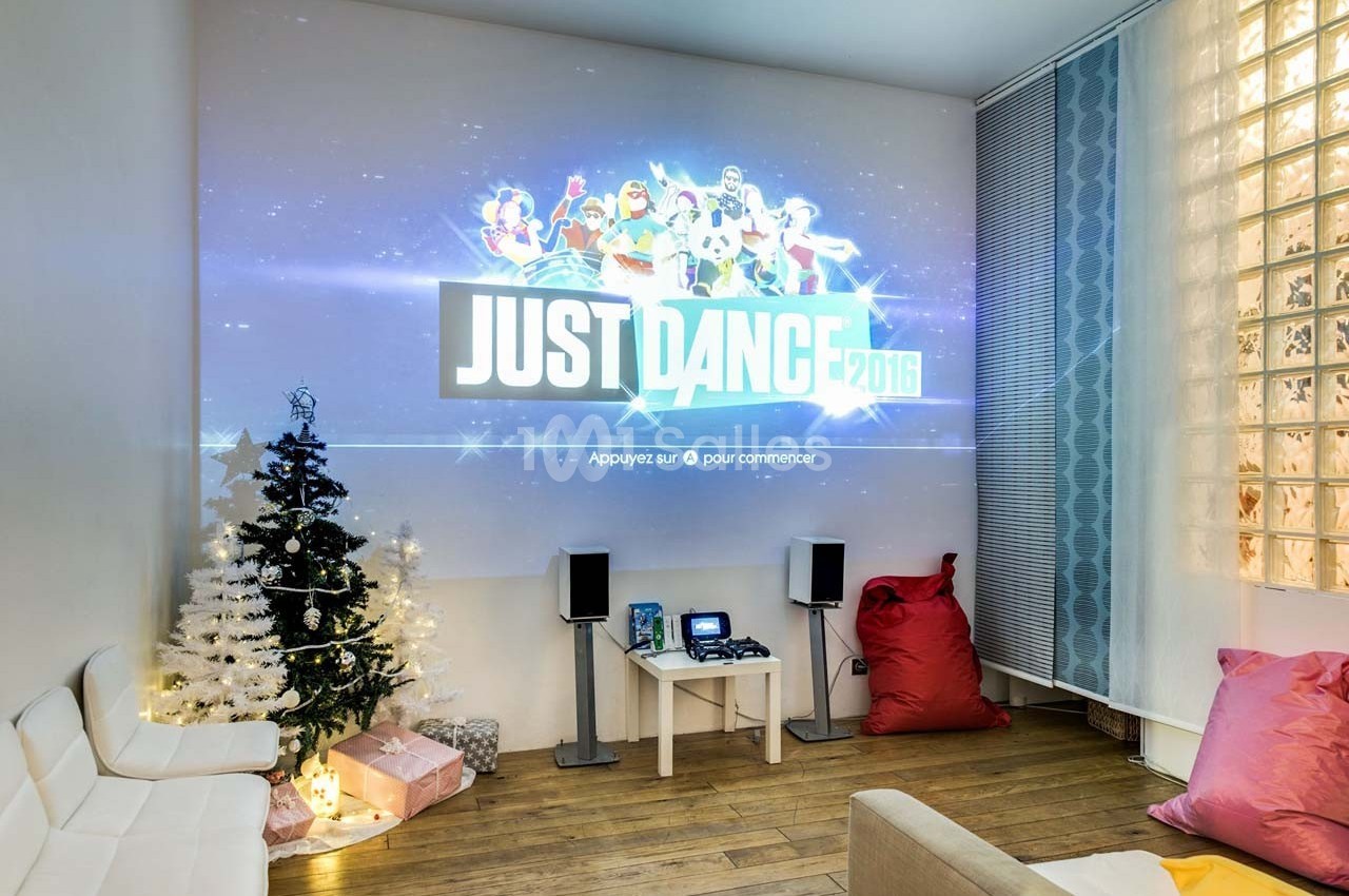 Projection du jeu ’Just Dance 2016’ sur un mur dans un salon décoré avec un sapin de Noël et des coussins colorés.