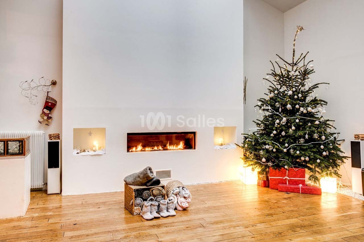 Salon chaleureux avec cheminée moderne, sapin de Noël décoré, cadeaux et chaussons posés sur un parquet en bois clair.