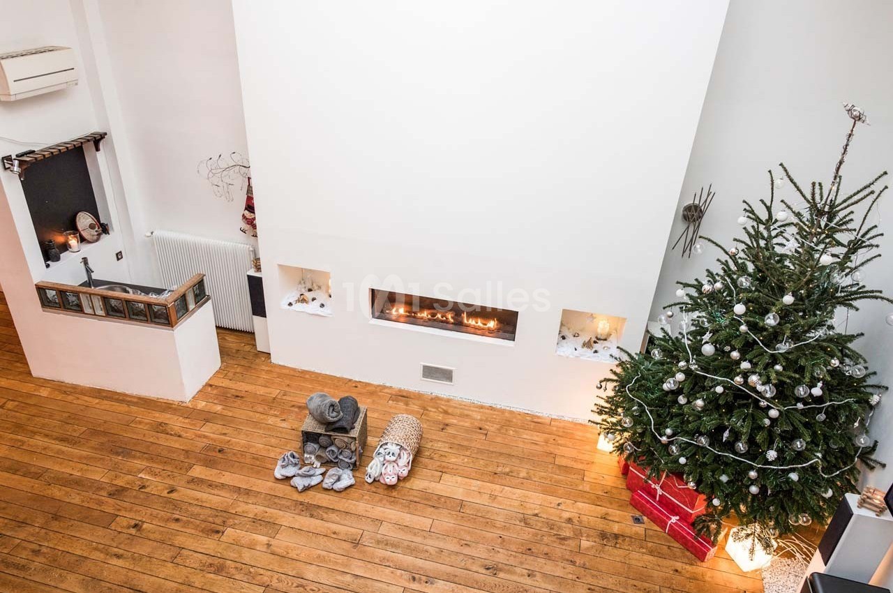 Salon avec parquet, cheminée moderne encastrée, sapin de Noël décoré et paniers contenant des plaids au sol.