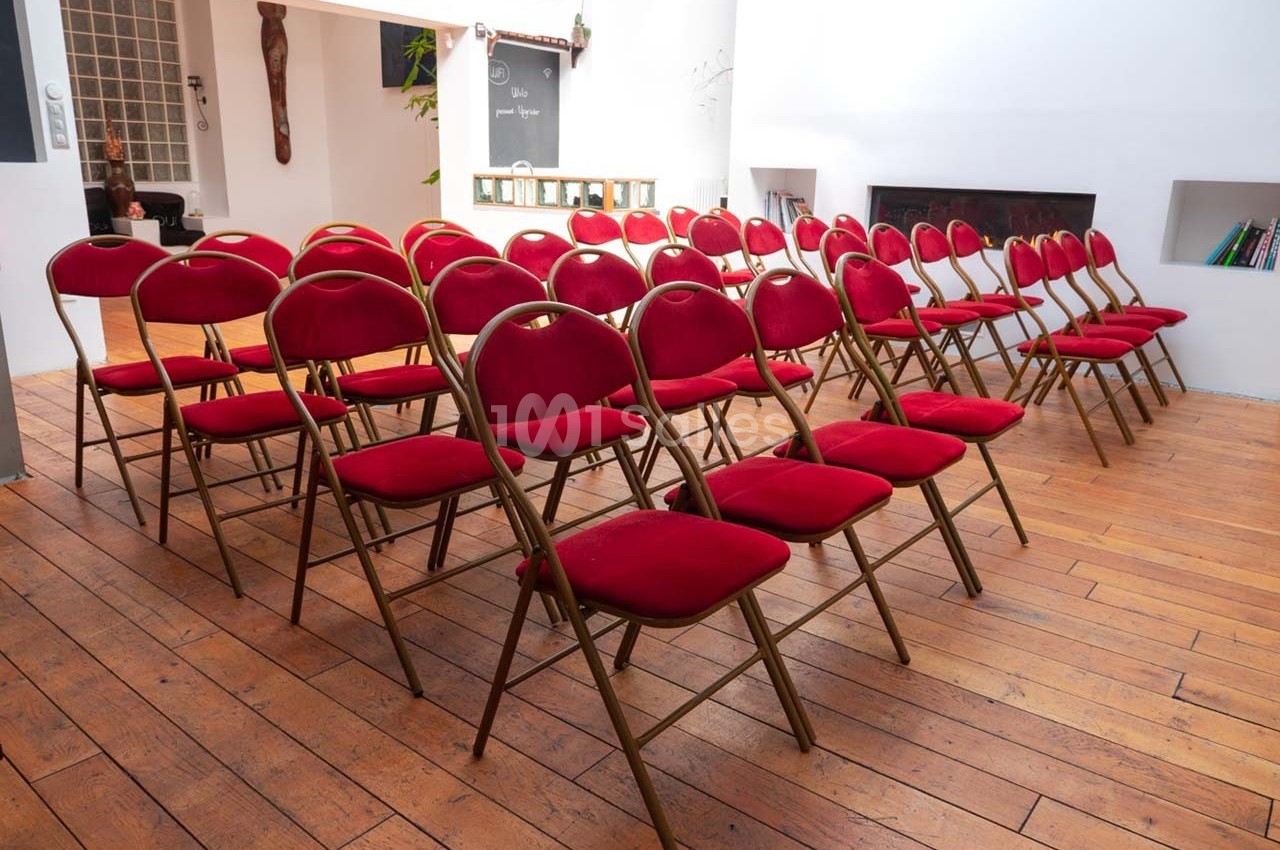 Rangées de chaises pliantes rouges alignées dans une salle lumineuse au sol en bois.