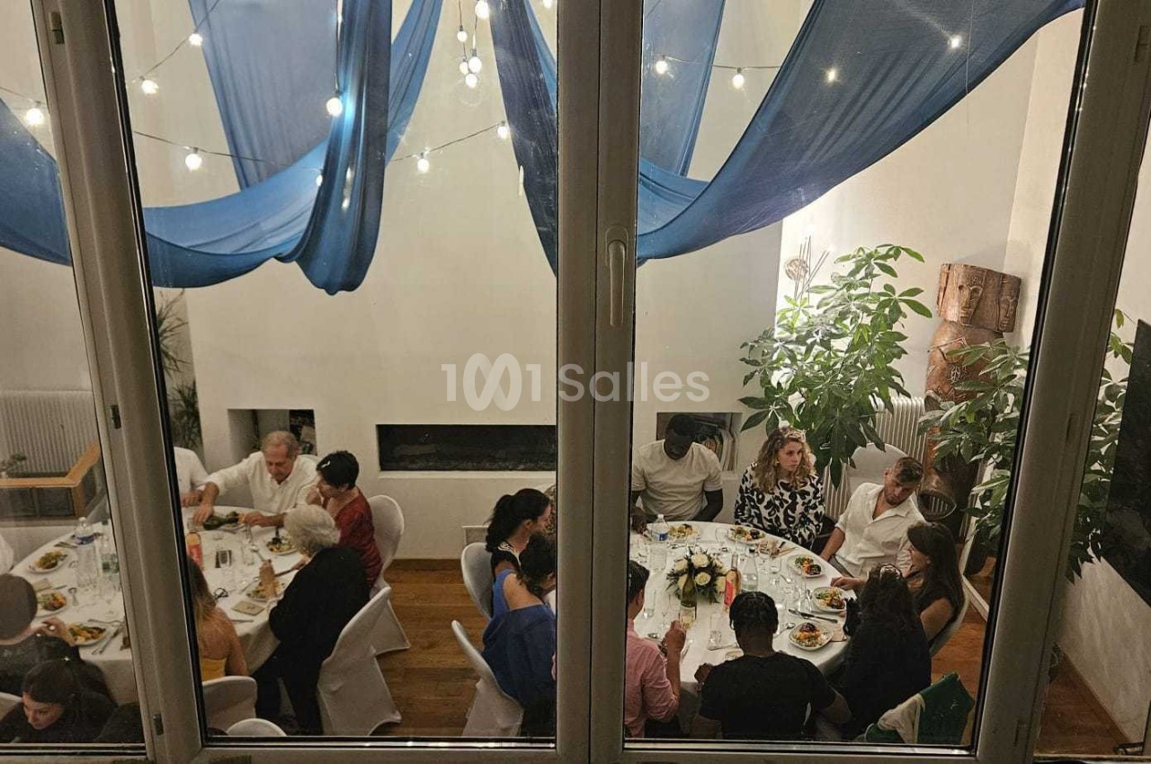 Vue à travers une fenêtre d'un dîner convivial avec plusieurs personnes assises autour de tables décorées.