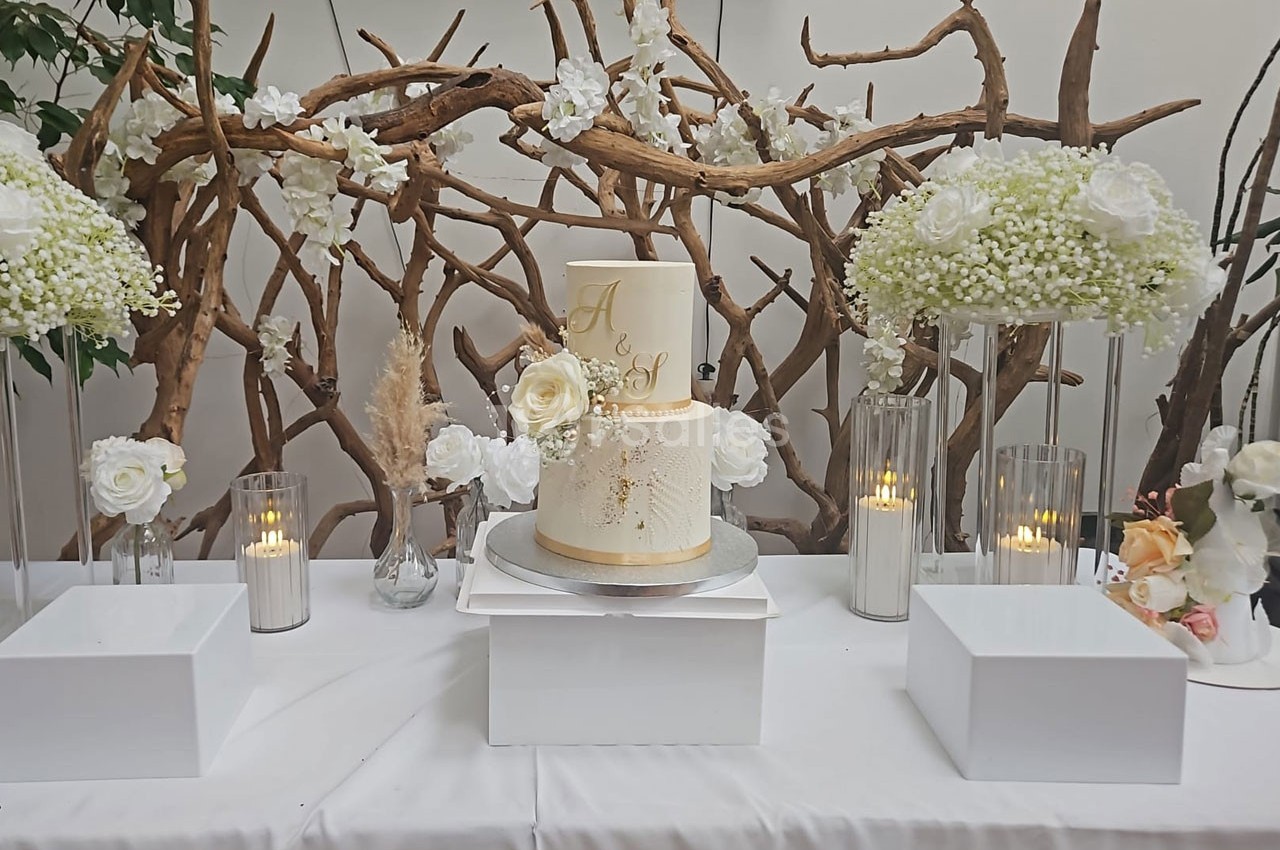 Gâteau de mariage décoré de fleurs blanches, entouré de bougies et de compositions florales sur une table blanche.