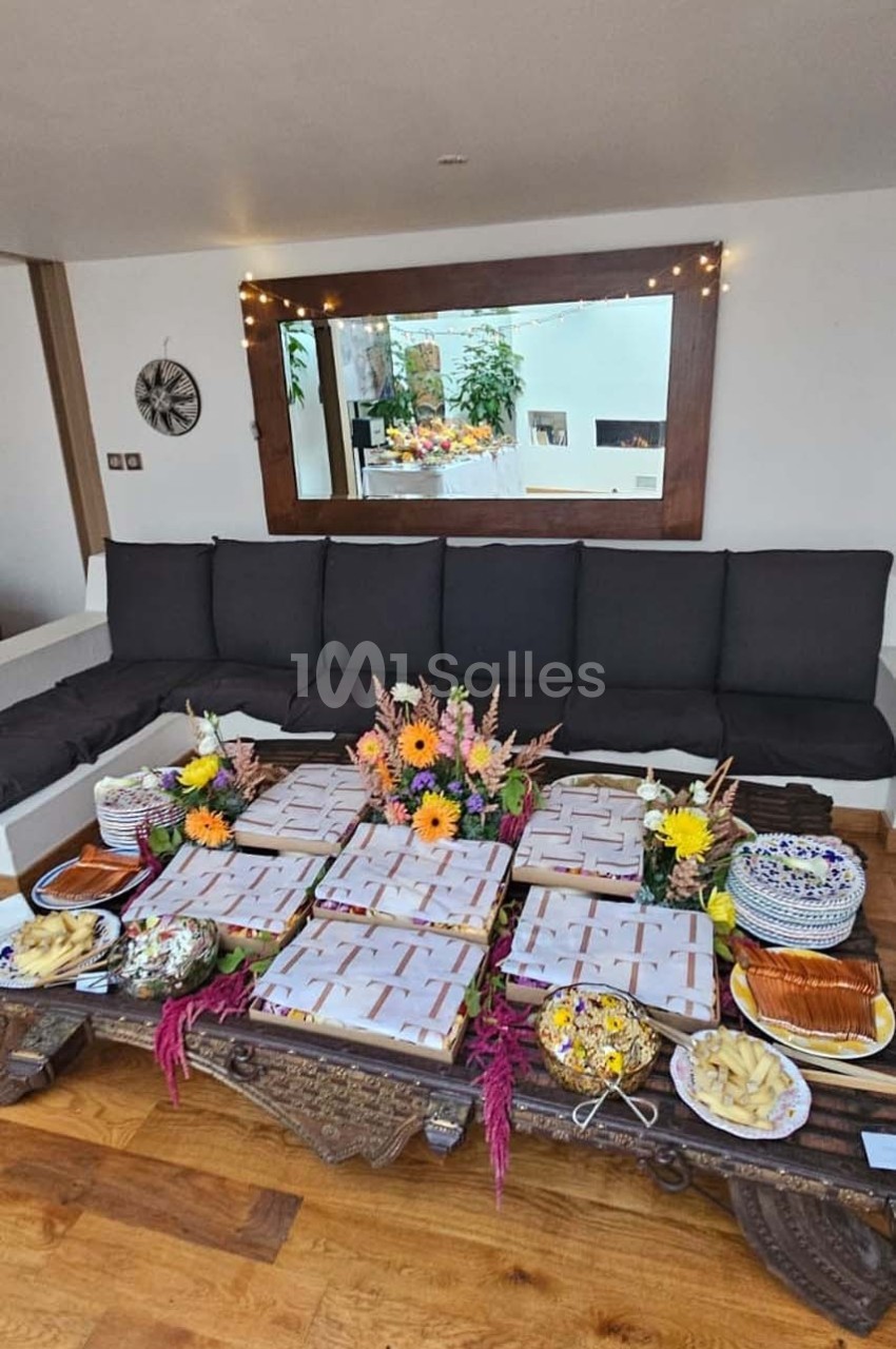 Plateau en bois avec des boîtes alignées, entouré de fleurs et de plats variés, dans un salon lumineux.