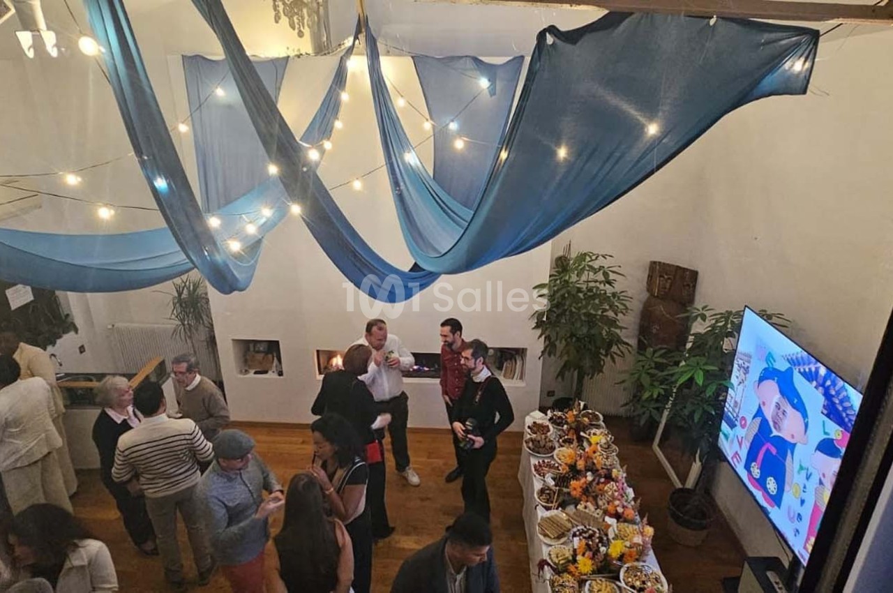 Des personnes discutent dans une salle décorée de voiles bleus, avec un buffet et un écran affichant une image colorée.