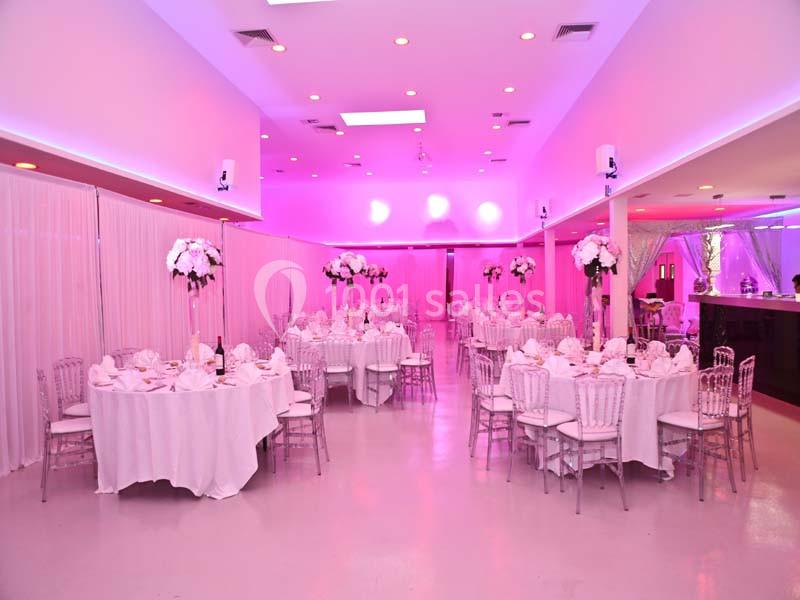 Salle de réception décorée avec des tables rondes dressées, des chaises transparentes et des centres de table fleuris.