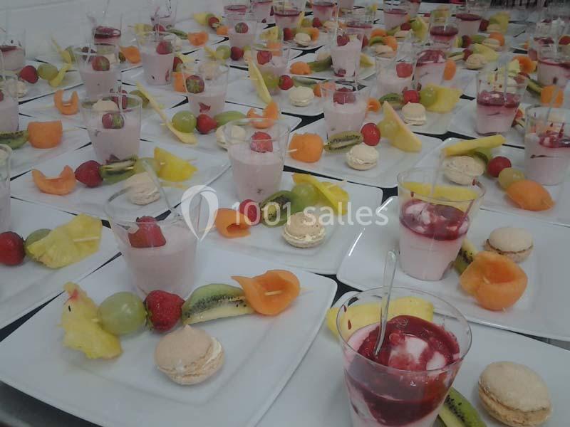 Assortiment de desserts avec verrines, fruits frais, macarons et coulis, disposés sur des assiettes blanches.