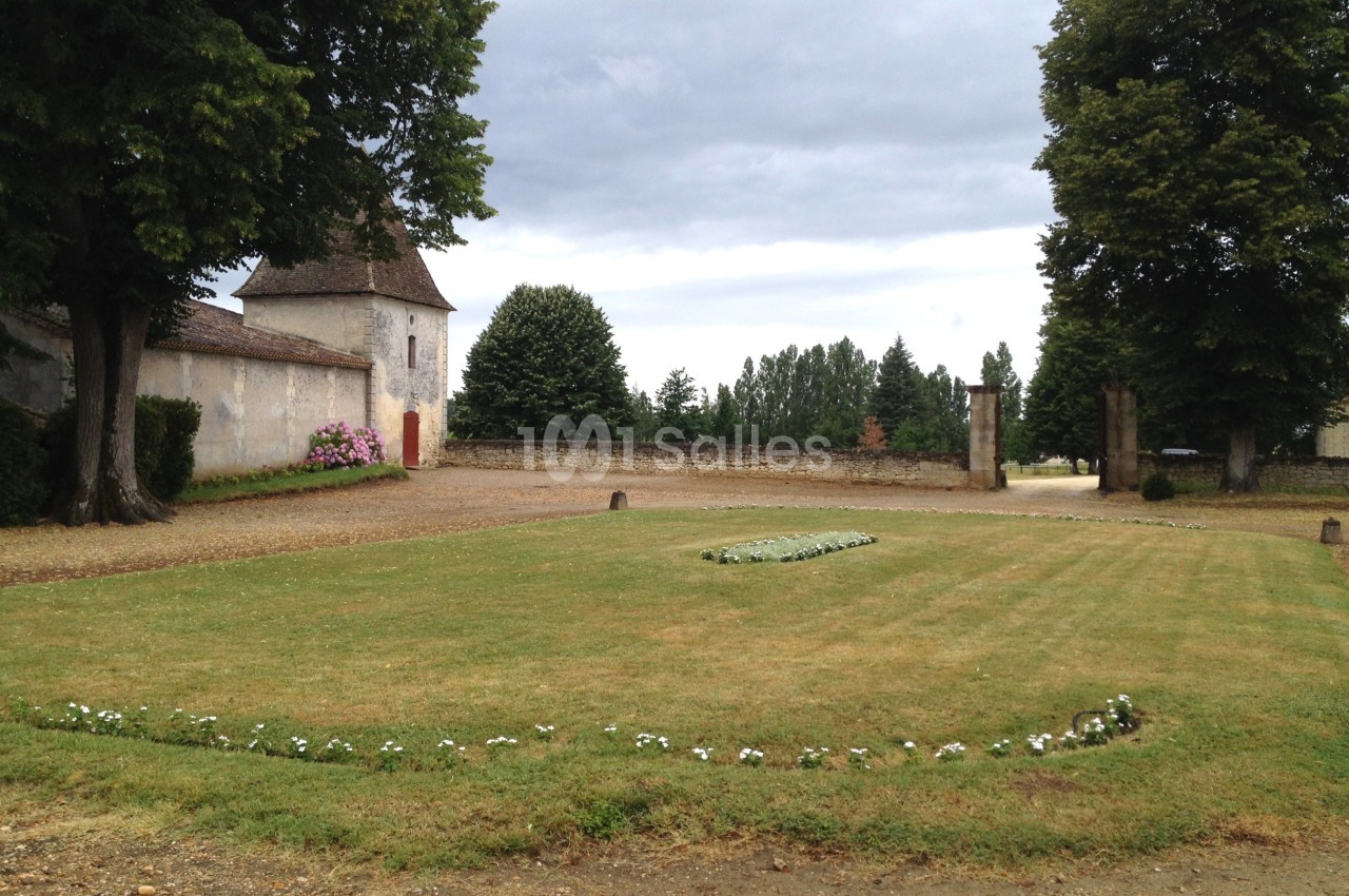 Pelouse entretenue avec parterre de fleurs, bordée d'arbres et d'un bâtiment ancien sous un ciel nuageux.