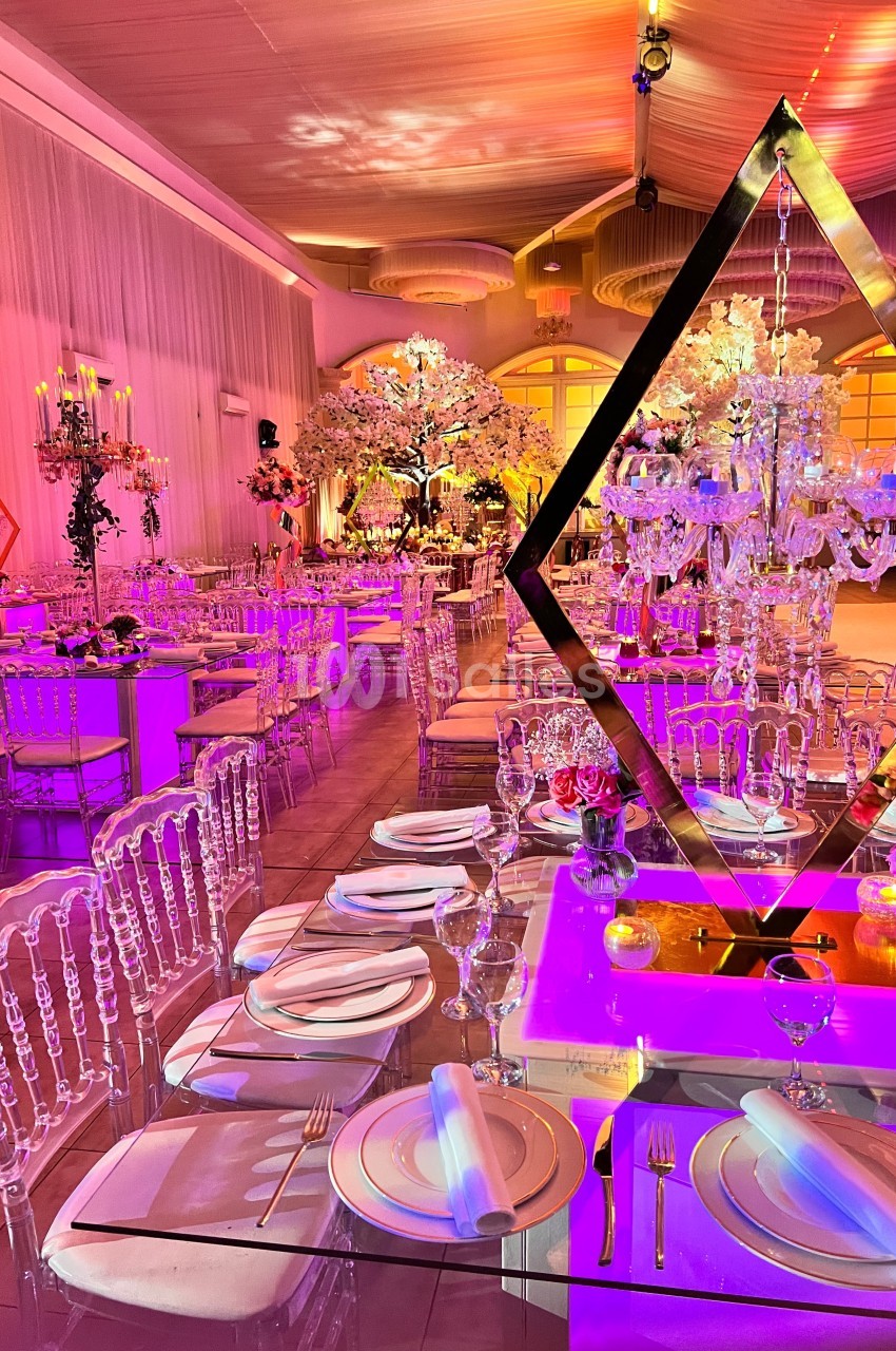 Salle de réception élégante avec tables dressées, chaises transparentes et éclairage coloré mettant en valeur des…