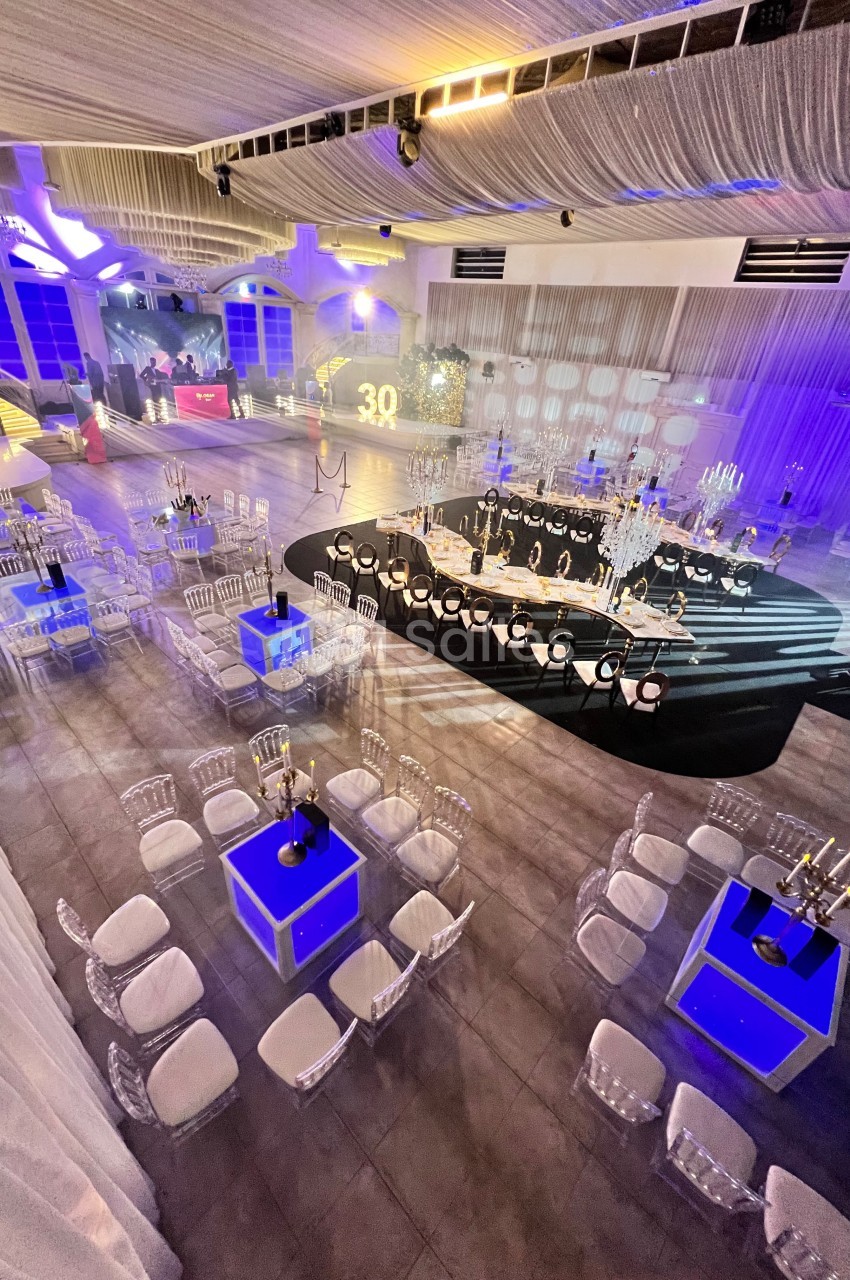 Salle de réception décorée avec des tables, chaises transparentes et éclairages bleus et blancs pour un événement.