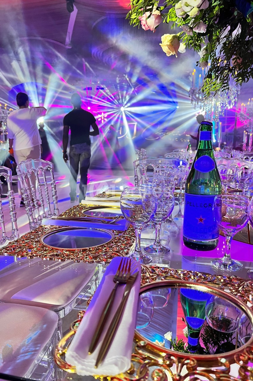 Table élégamment dressée avec des assiettes dorées, vue sur une piste de danse illuminée par des jeux de lumière colorés.