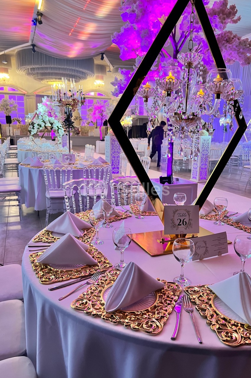 Salle de réception décorée avec des tables élégantes, nappes blanches, chandeliers et éclairage rose.