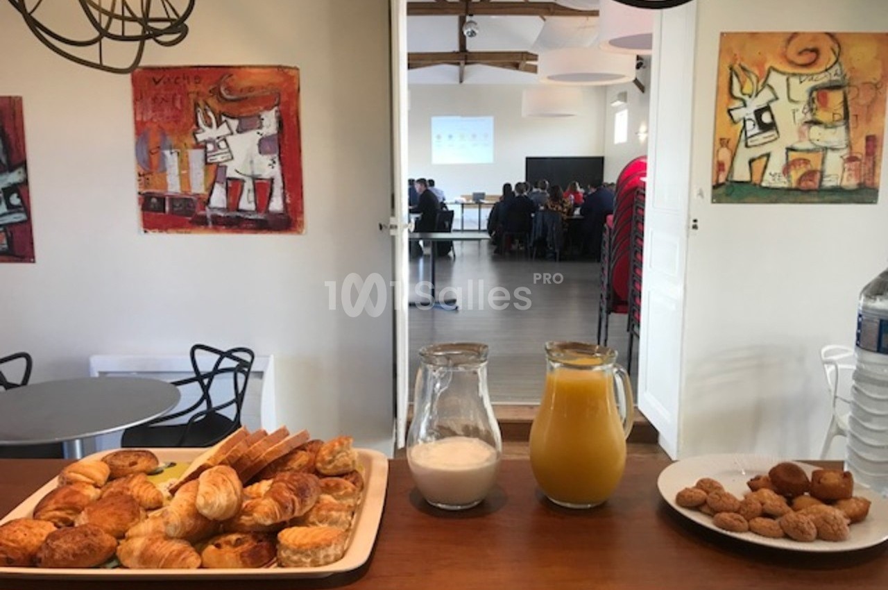 Plateau de viennoiseries, carafe de jus d'orange, lait et biscuits disposés sur un comptoir dans une salle de réunion.