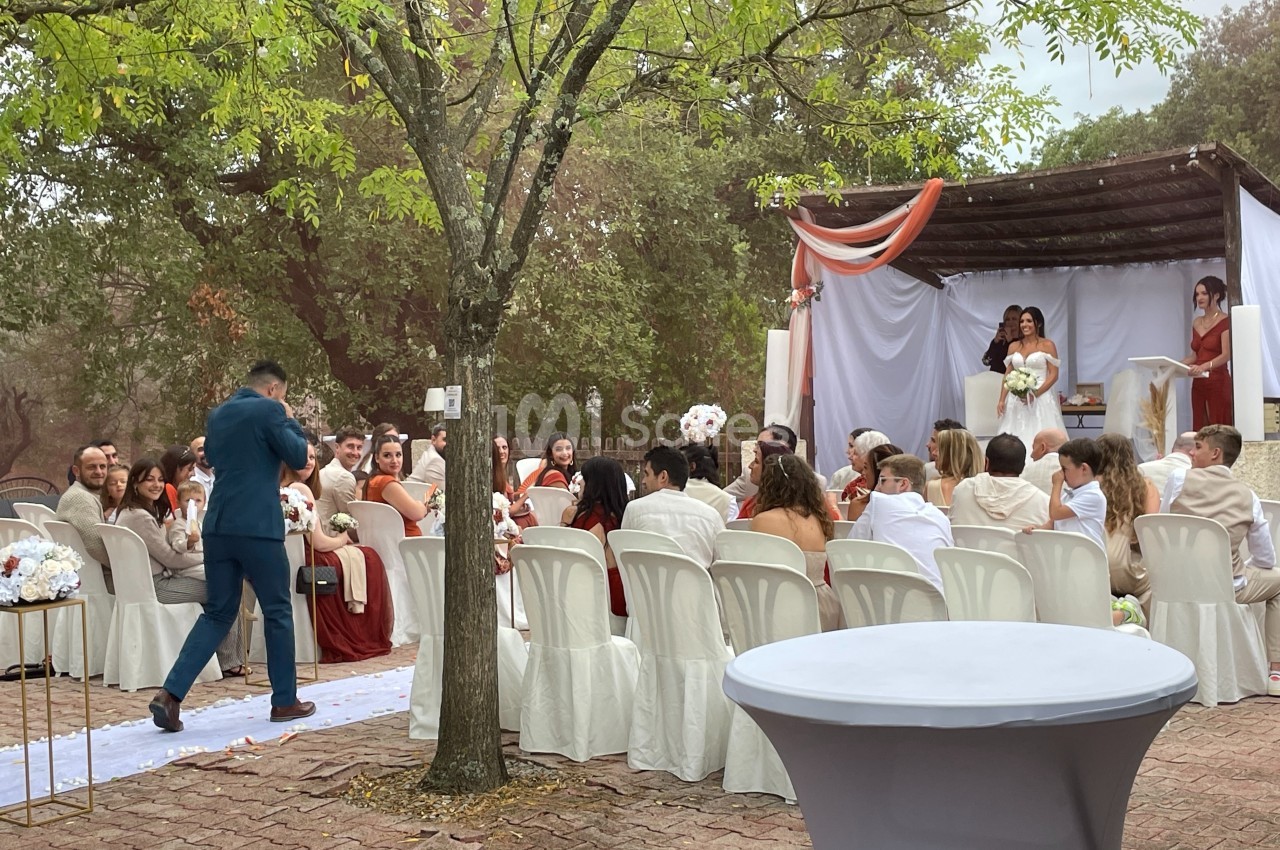 Cérémonie de mariage en plein air avec invités assis, décorations blanches et rouges, et mariés sous une pergola.