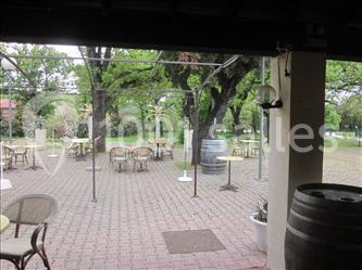 Terrasse extérieure avec tables et chaises vides, entourée d'arbres et de verdure, sous un ciel couvert.