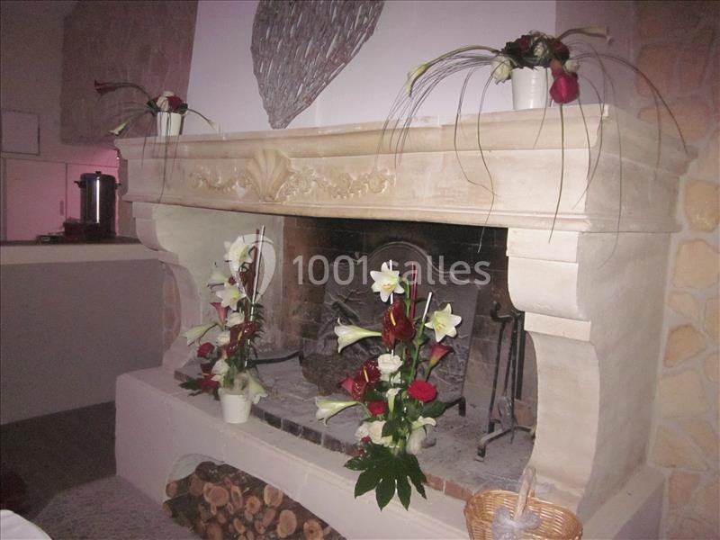 Cheminée en pierre décorée de bouquets de fleurs blanches et rouges, avec des bûches empilées en dessous.