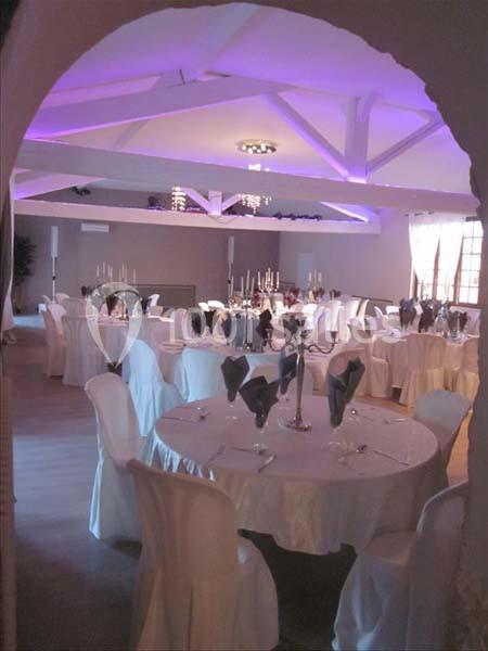 Salle de réception décorée avec des tables rondes, nappes blanches, serviettes pliées et éclairage tamisé violet.