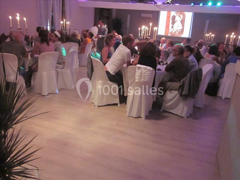 Des convives assis à des tables rondes dans une salle éclairée, décorée de chandeliers et d'une projection murale.