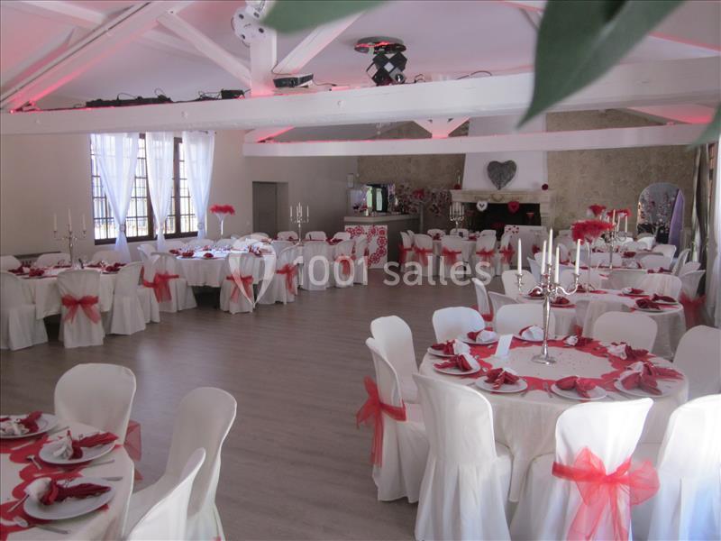 Salle de réception décorée avec des nappes blanches, des rubans rouges et des chandeliers sur les tables.