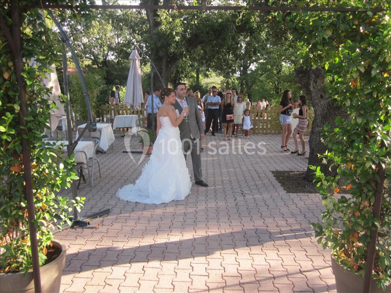 Un couple en tenue de mariage se tient debout dans une cour pavée entourée de verdure et d'invités.