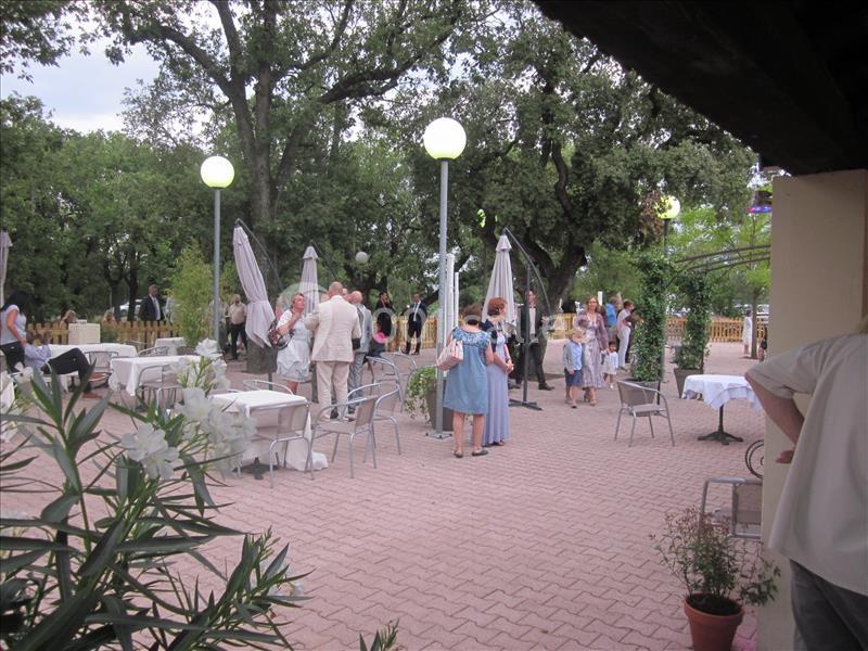 Personnes rassemblées sur une terrasse pavée avec des tables dressées, entourée de végétation et éclairée par des…