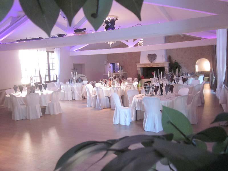 Salle de réception décorée avec des tables rondes dressées, nappes blanches et chandeliers, sous un éclairage tamisé.