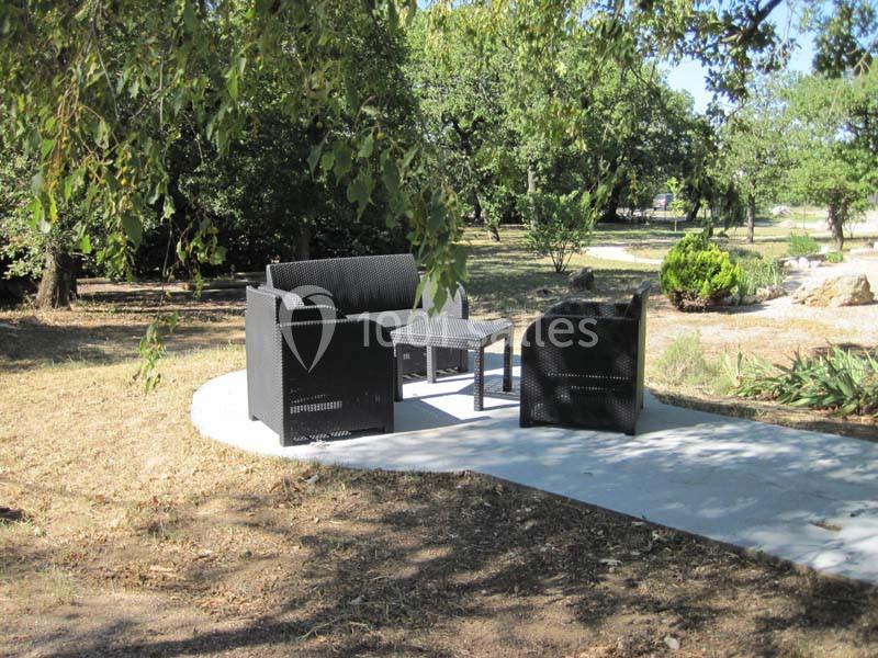 Mobilier de jardin en résine tressée disposé sur une terrasse en béton, entouré d'arbres et de verdure.