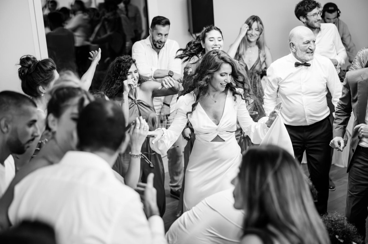 Personnes dansant joyeusement lors d'une fête, avec une femme en robe blanche au centre de l'attention.