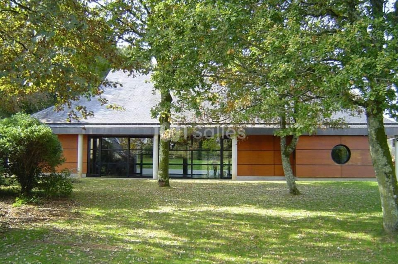 Bâtiment moderne avec façade en bois et grandes baies vitrées, entouré d'arbres et d'une pelouse.