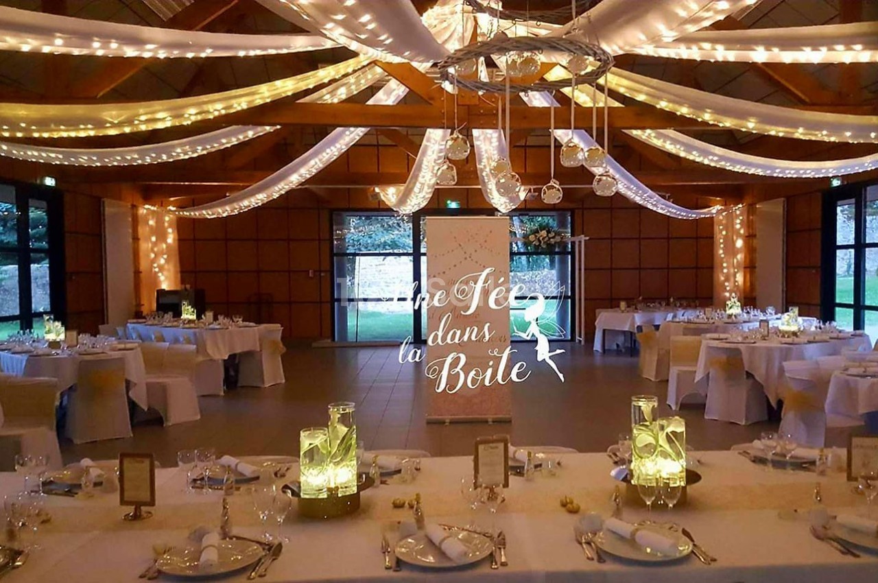 Salle de réception décorée avec des guirlandes lumineuses, des tables dressées et un panneau lumineux au centre.
