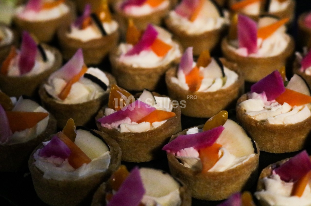 Petites tartelettes garnies de fromage frais et décorées de légumes colorés, présentées en rangées serrées.