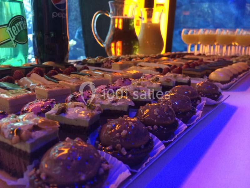 Plateau de desserts variés avec gâteaux, pâtisseries et verrines, disposés sur une table éclairée.