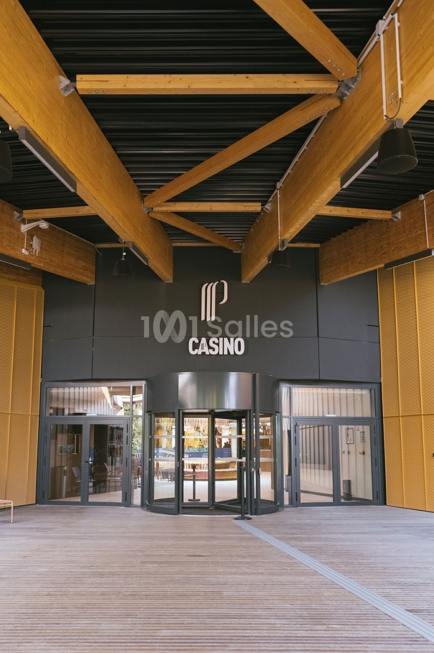 Entrée principale d'un casino moderne avec des structures en bois et un logo visible au-dessus des portes vitrées.