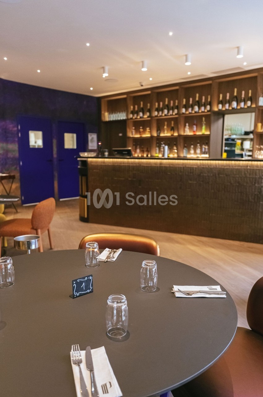 Table dressée avec couverts et verres dans un restaurant moderne, avec un bar en arrière-plan.