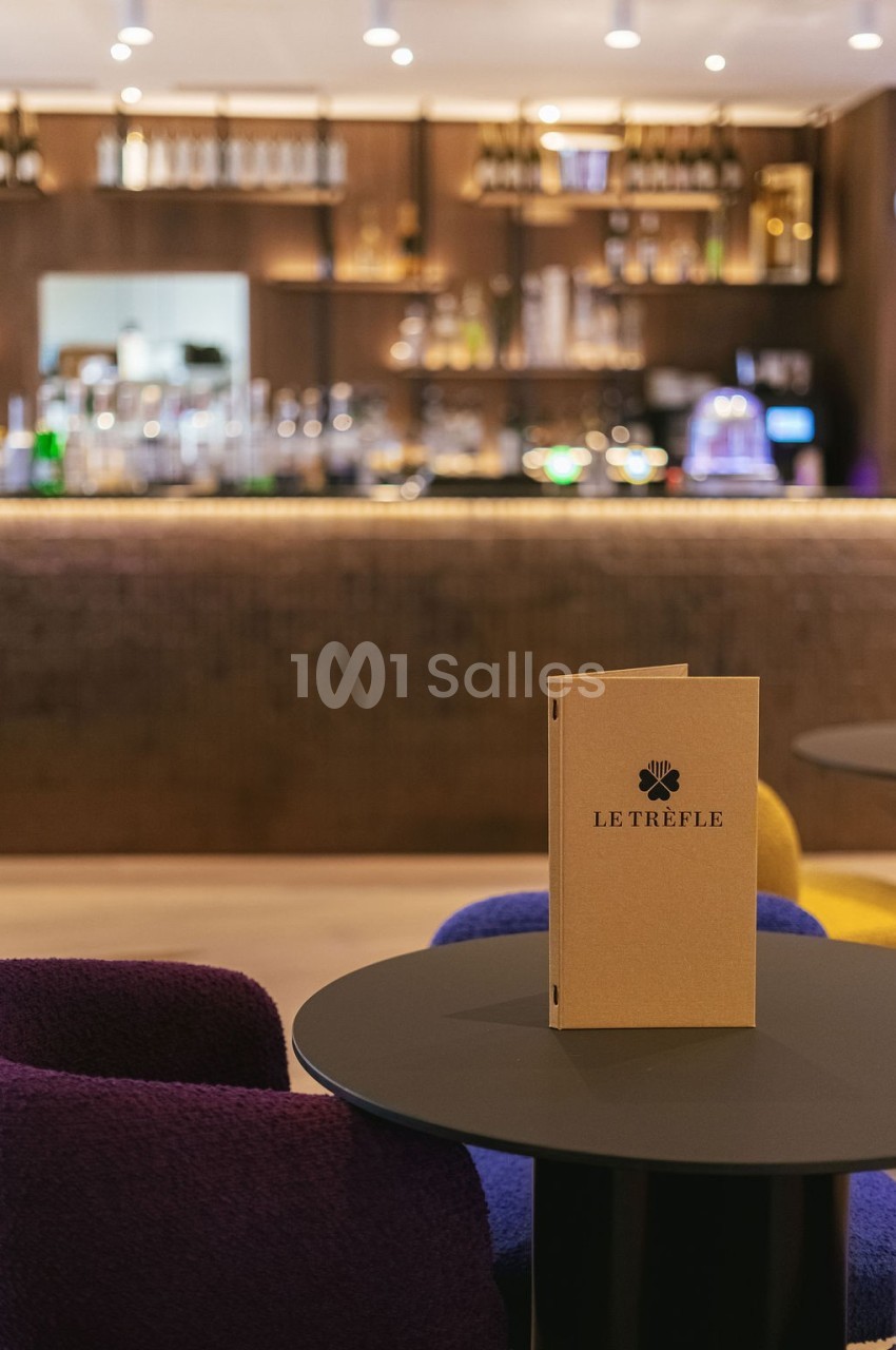 Menu posé sur une table ronde dans un bar élégant avec un comptoir éclairé en arrière-plan.