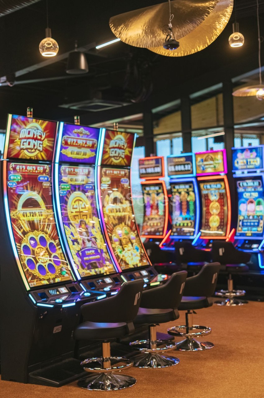 Rangée de machines à sous colorées alignées dans un casino, avec des sièges noirs devant chaque machine.